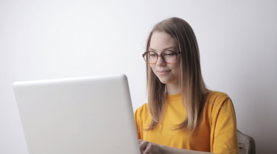 Young woman with glasses working on a laptop, focused and smiling.
