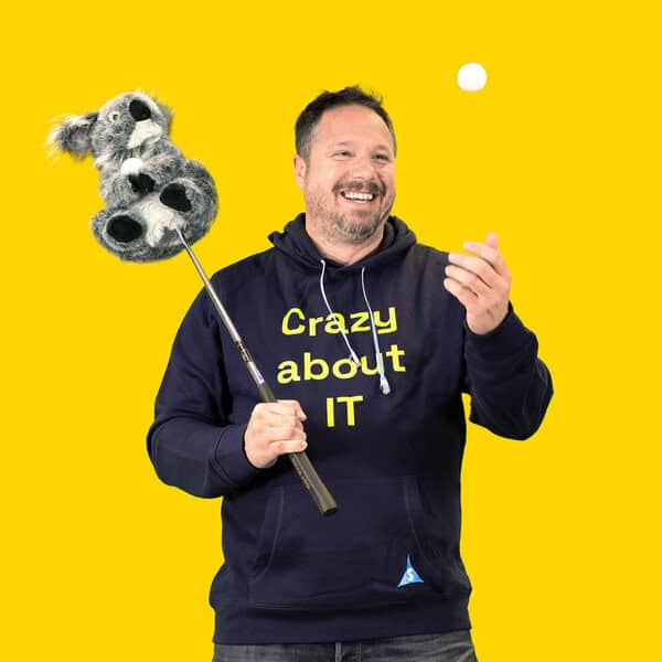 Man holding a koala plush toy with a yellow background, smiling.